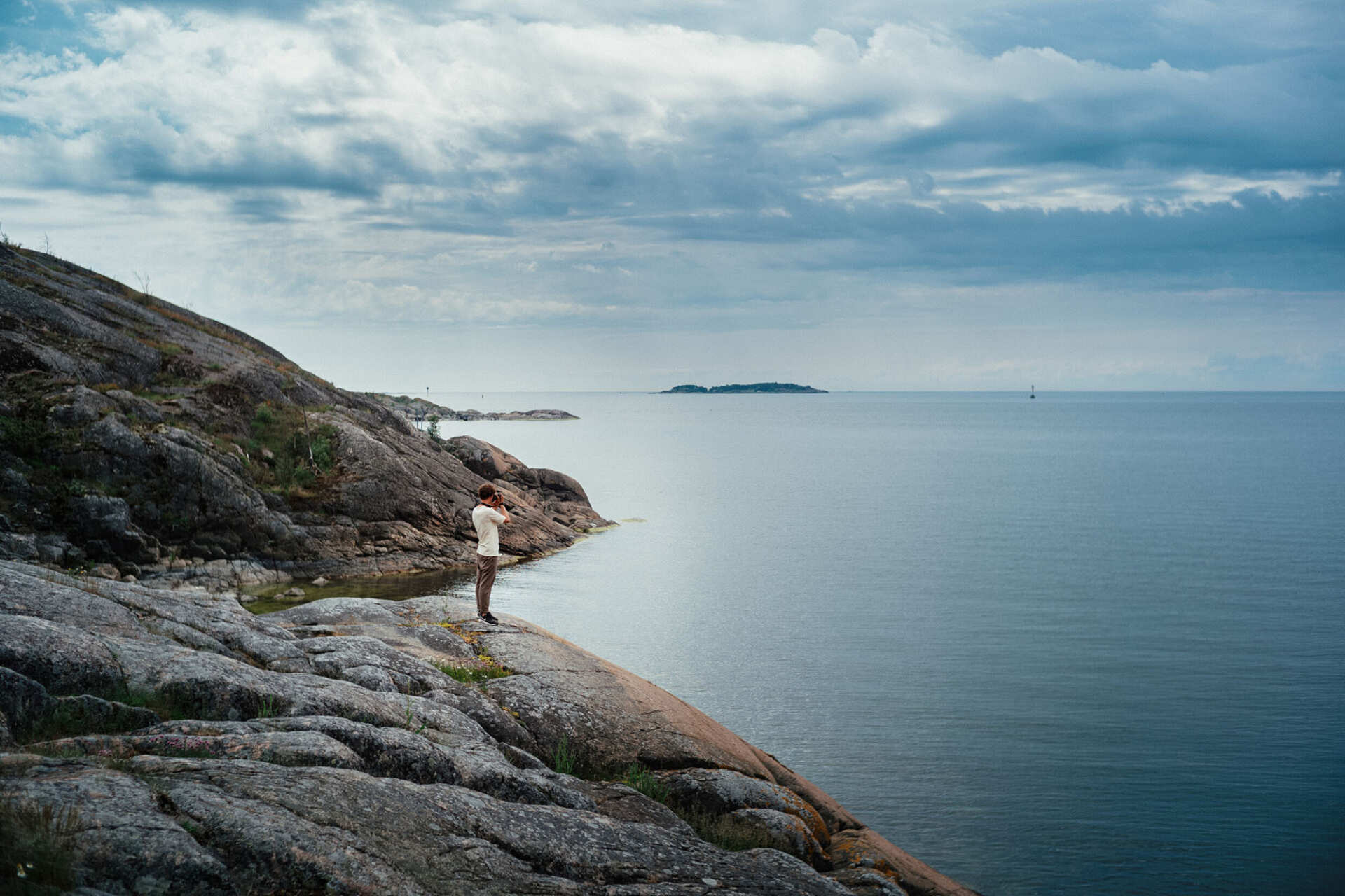 A man holding a camera and standing on a cliff by the sea