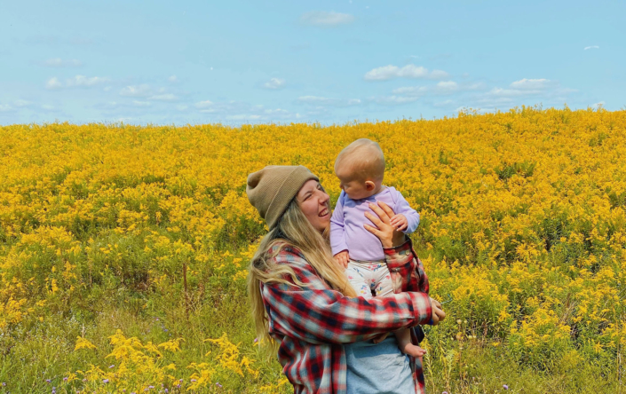 Mother holding a baby, yellow flower field in the background